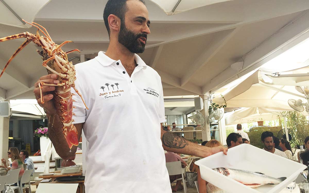 Waiter from Juan & Andrea's, one of Formentera's premier lunch spots, holding a live lobster and fresh fish 