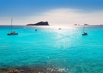 Four yachts at anchor at Cala Tarida in the turquoise blue waters at sunrise in Ibiza