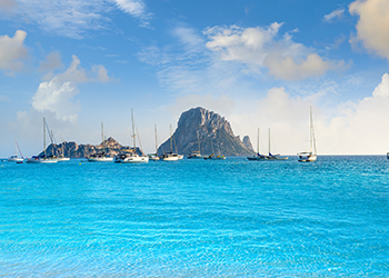 Es Vedra surrounded by yachts in the the bluest of seas viewed from a boat chartered in Ibiza and Formentera